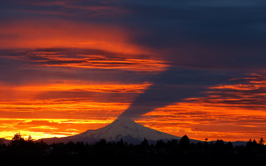The shape of Mount Hood is cast as a shadow as the sun rises through clouds near Portland, Oregon